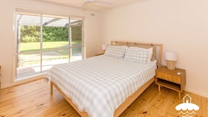 Une chambre avec une grande fenêtre, un lit en bois, des tables de chevet et un ventilateur de plafond.