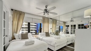 Habitación de hotel con dos camas, ventilador de techo, un espejo grande y vista a la ciudad.