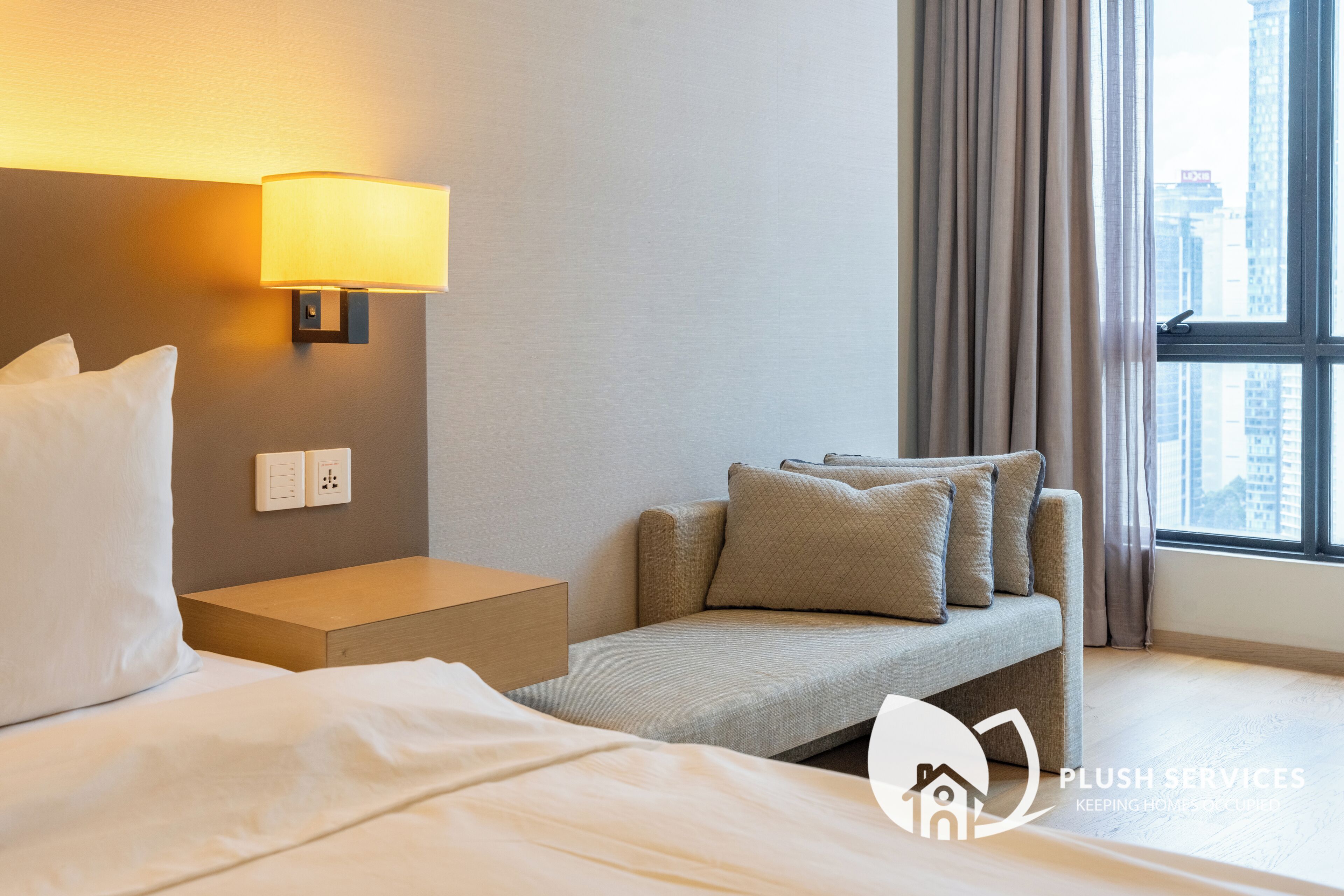 Une chambre d’hôtel avec un lit, une table de chevet, une lampe, un canapé et une fenêtre avec des rideaux.