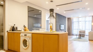 A modern kitchen with a built-in washing machine, a dining area with a sofa and a chair, and a large window with curtains. - Premium 188 Residence (Kuala Lumpur)