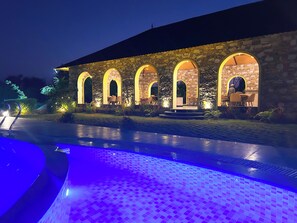A stone building with arched windows and a pool area with blue lighting. - Jawai's Wildness Lodge (Bali)