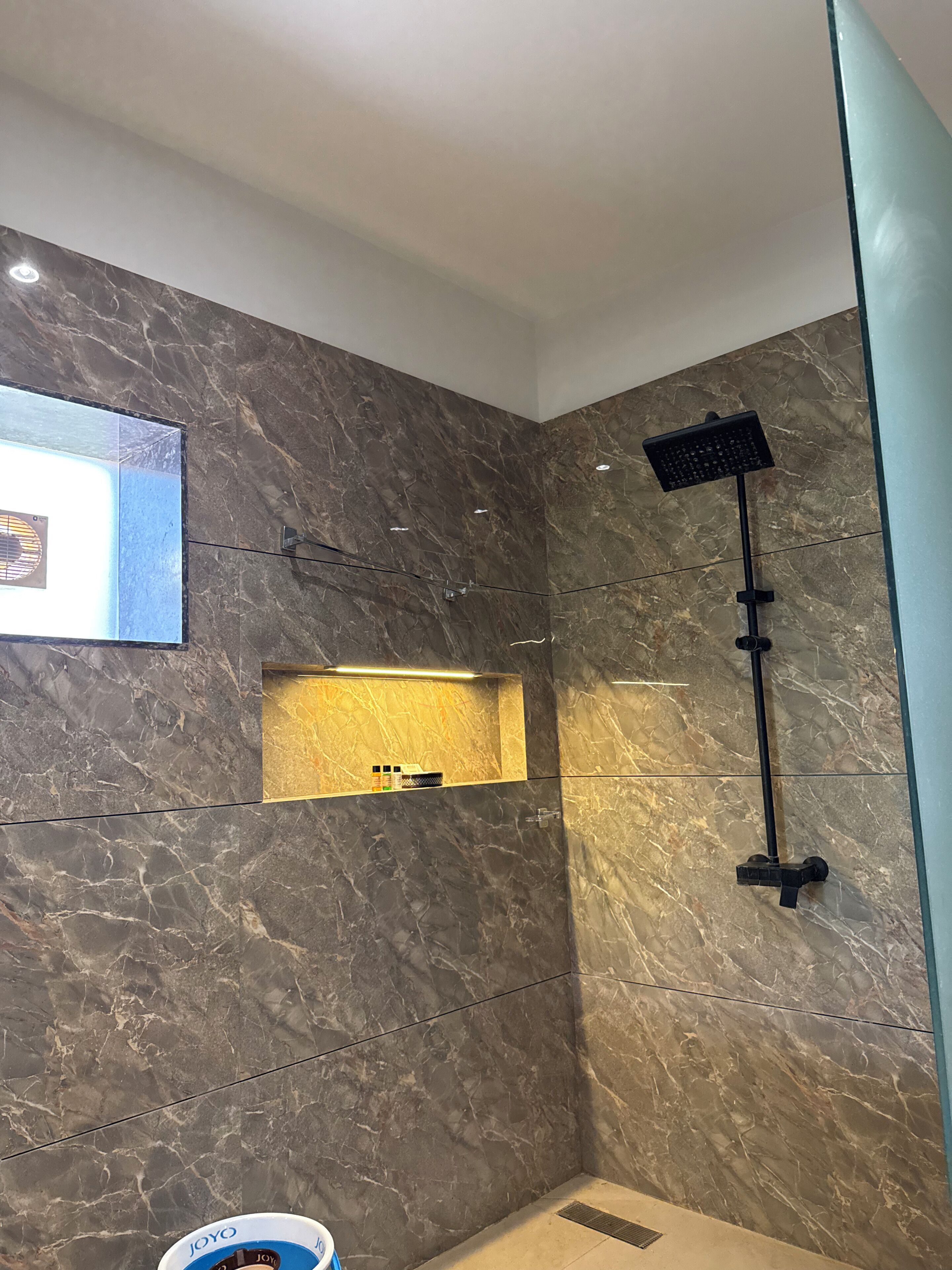 A modern bathroom with a marble wall, a built-in shelf with toiletries, and a handheld showerhead.
