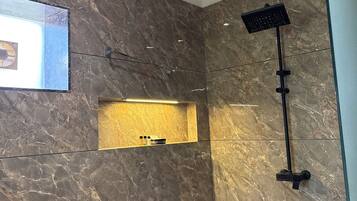 A modern bathroom with a marble wall, a built-in shelf with toiletries, and a handheld showerhead.