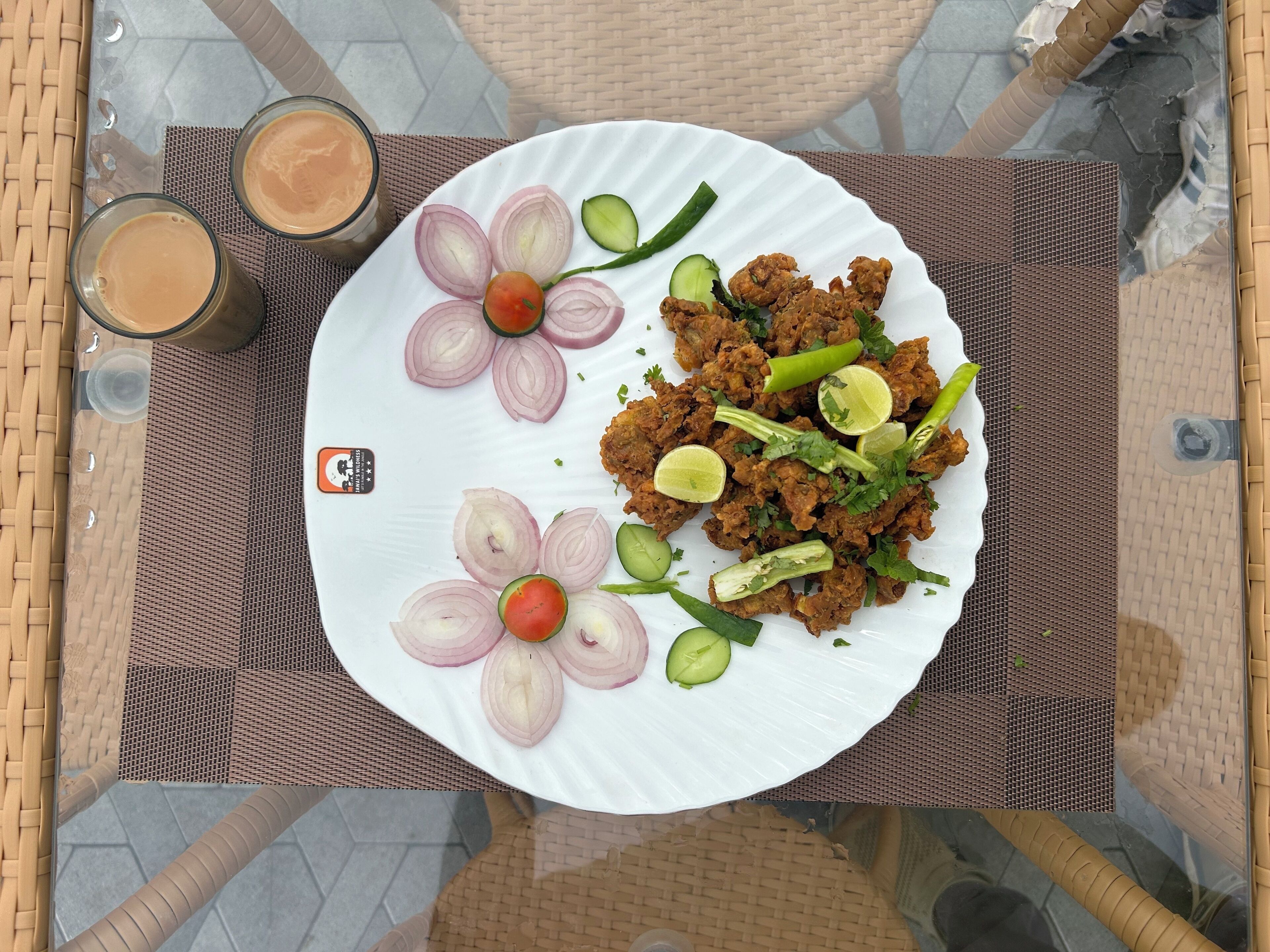 A dining table with a plate of food, two glasses of a brown beverage, and a woven placemat.