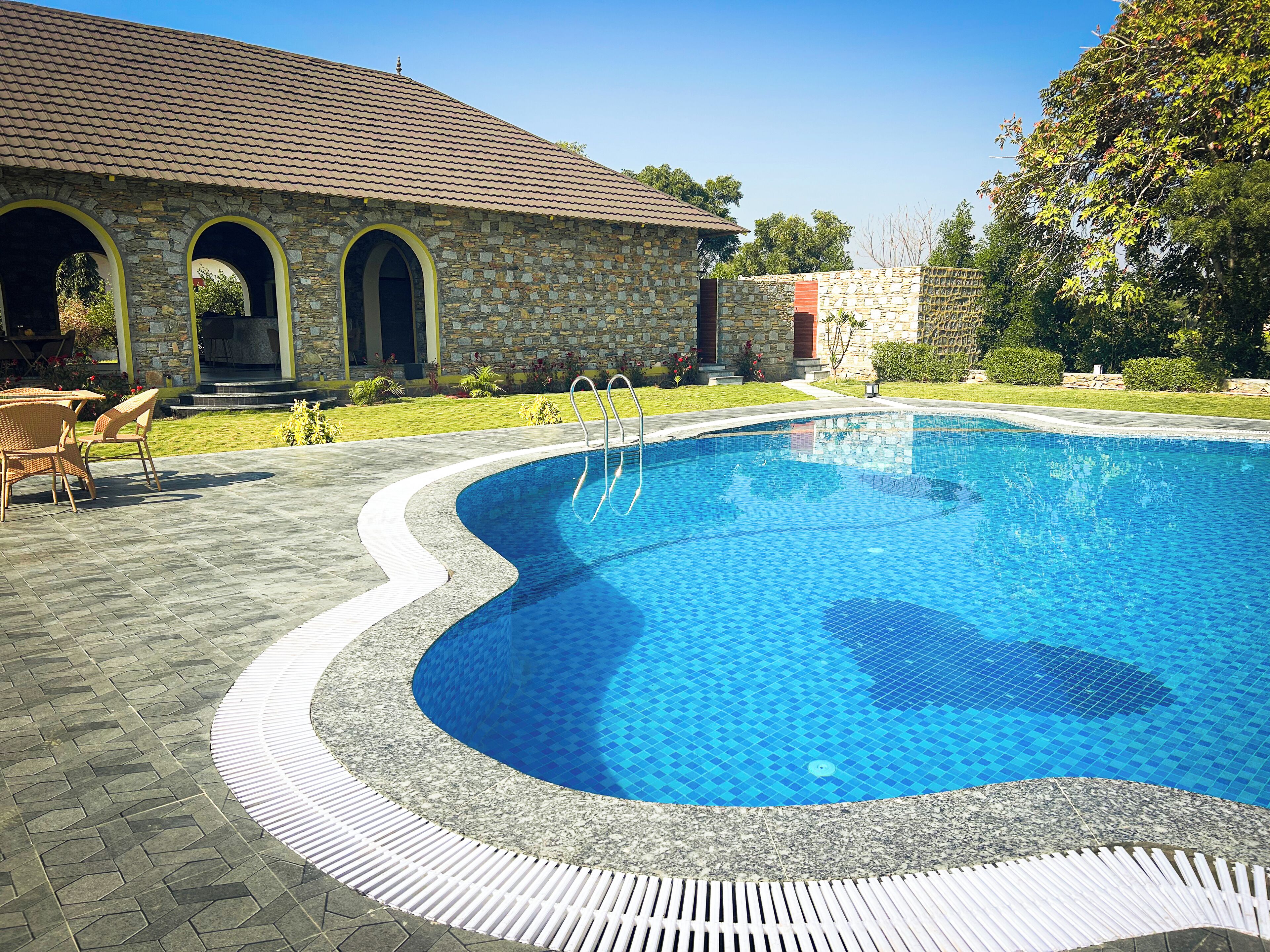 Ein Pool mit Steinmauer und Rundbogen, umgeben von einer Terrasse mit Stühlen.