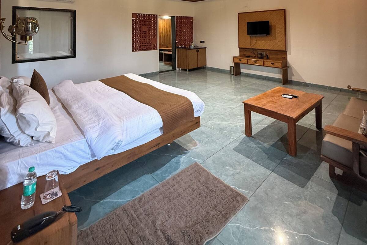 A modern hotel room with a large bed, a flat-screen TV, a wooden coffee table, and a ceiling fan.