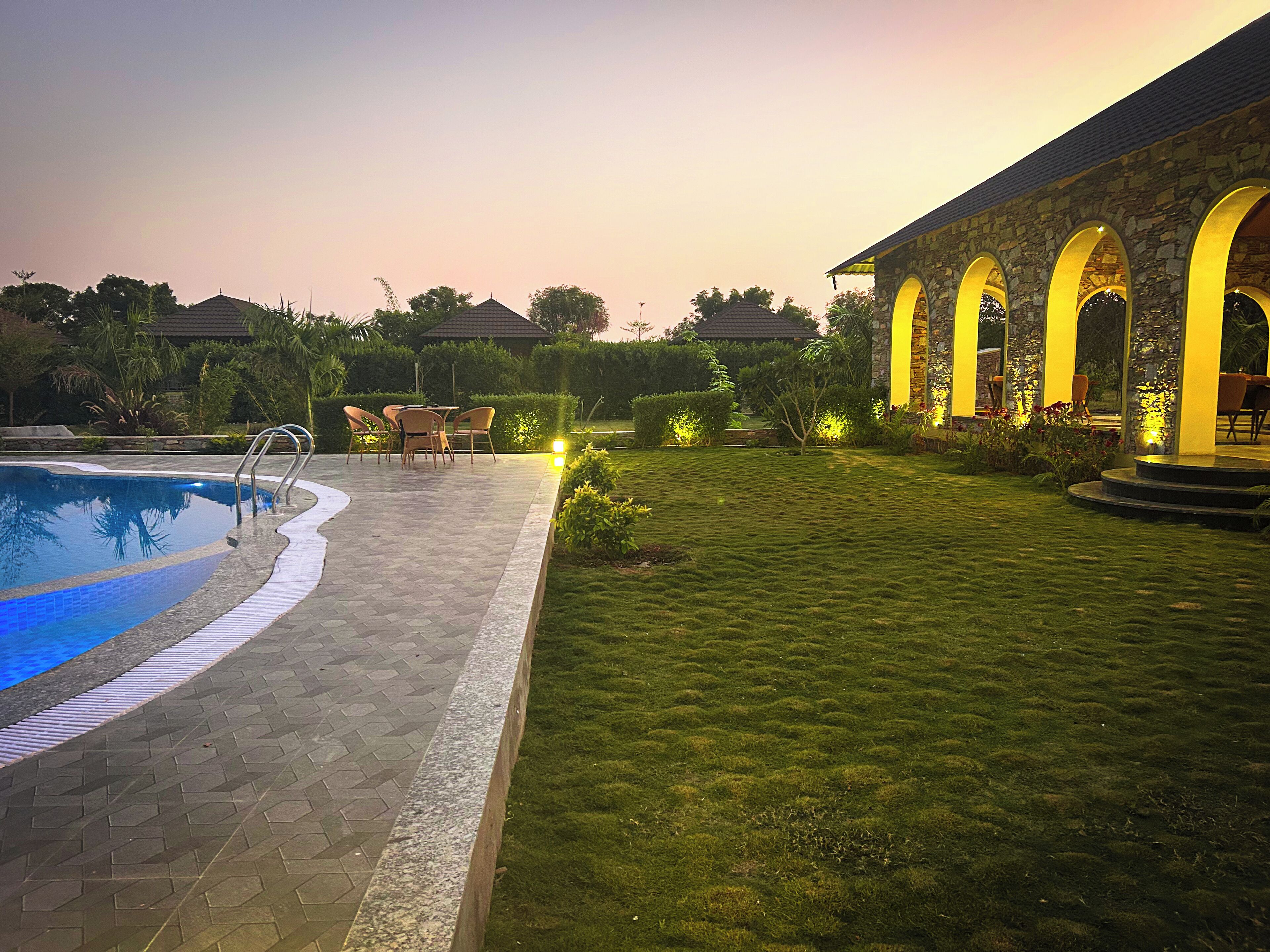 A swimming pool with a tiled deck, a grassy lawn, and a stone building with arched windows.