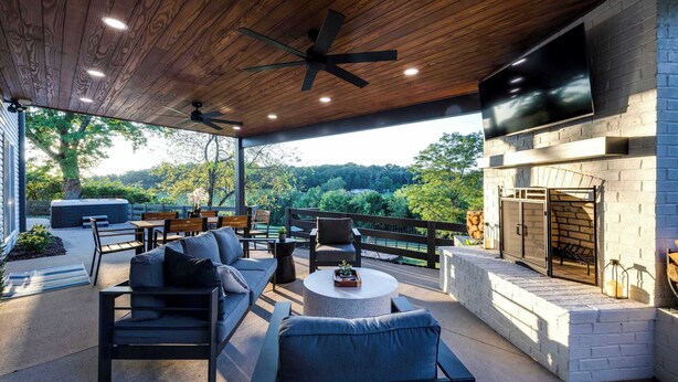 Eine Terrasse im Freien mit modernem Design, ausgestattet mit einem Steinkamin, bequemen Sitzgelegenheiten und einem großen Fernseher.