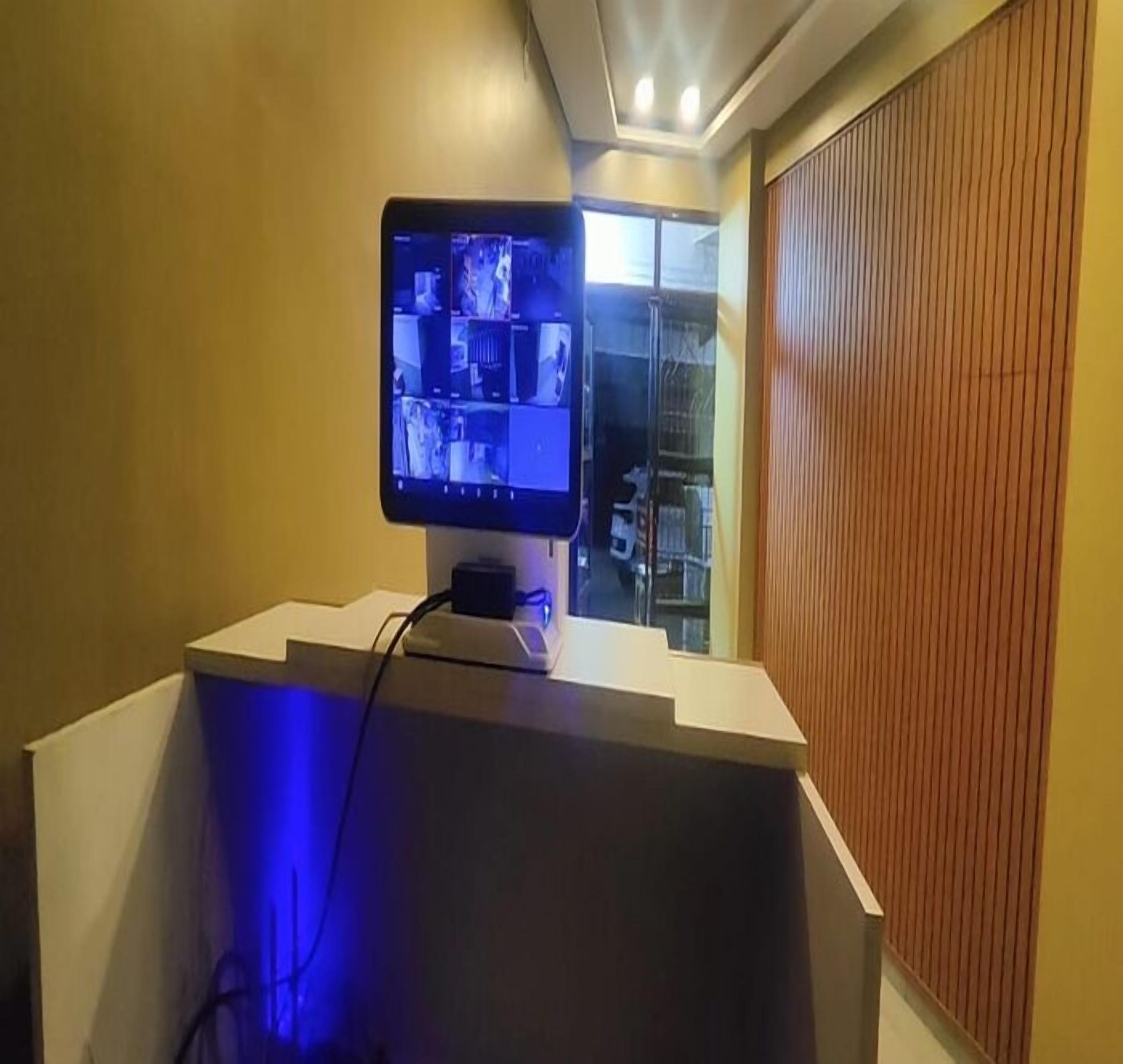 A room with a monitor displaying multiple screens, a white desk, and a wooden panel on the right.