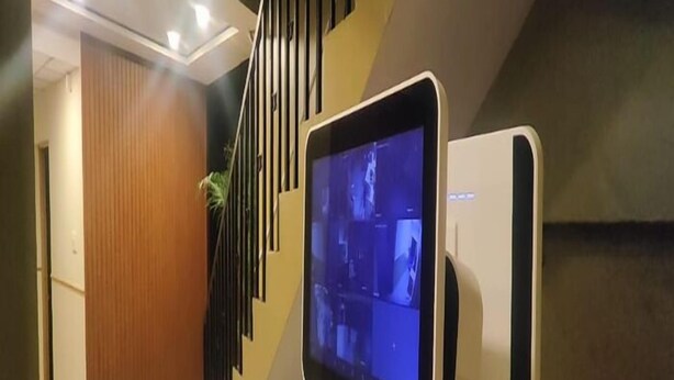 A modern interior with a staircase, a mounted screen displaying content, and a wooden door. - Diya residence (Mysore)