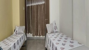 A small, clean room with two single beds, a curtain, and a tiled floor. - Diya residence (Mysore)