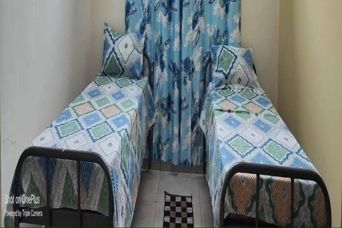 Une petite pièce étroite avec deux lits simples, chacun agrémenté de draps à motifs. Un rideau orné de motifs floraux recouvre la fenêtre.