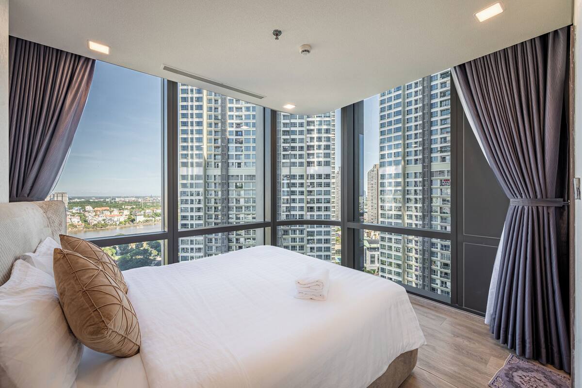 Une chambre d’hôtel moderne avec un grand lit, une vue sur les gratte-ciel et un balcon agrémenté de rideaux.