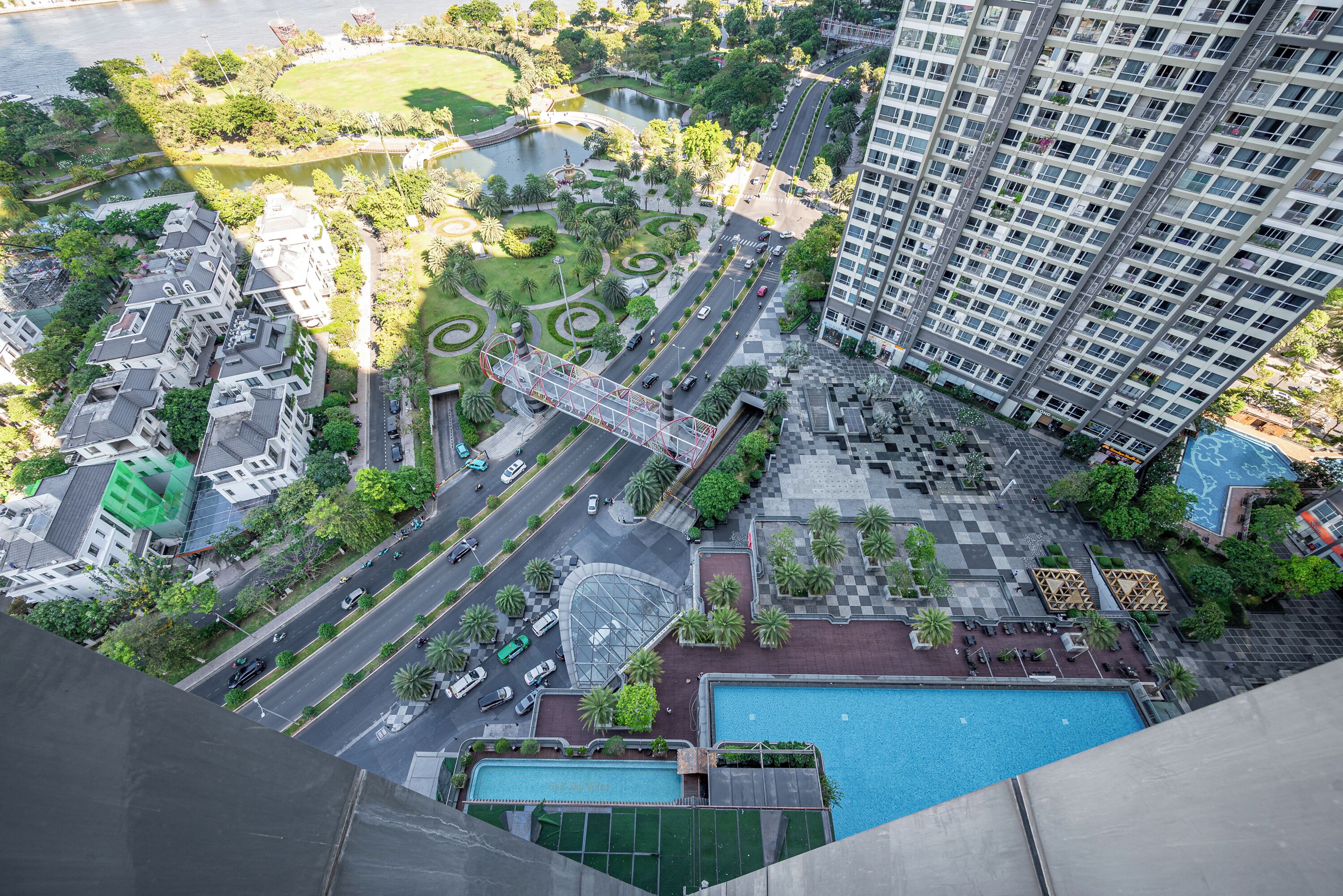 A high-rise building with a rooftop pool and a landscaped park area with pathways and greenery.