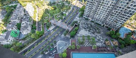 A high-rise building with a rooftop pool and a landscaped park area with pathways and greenery.