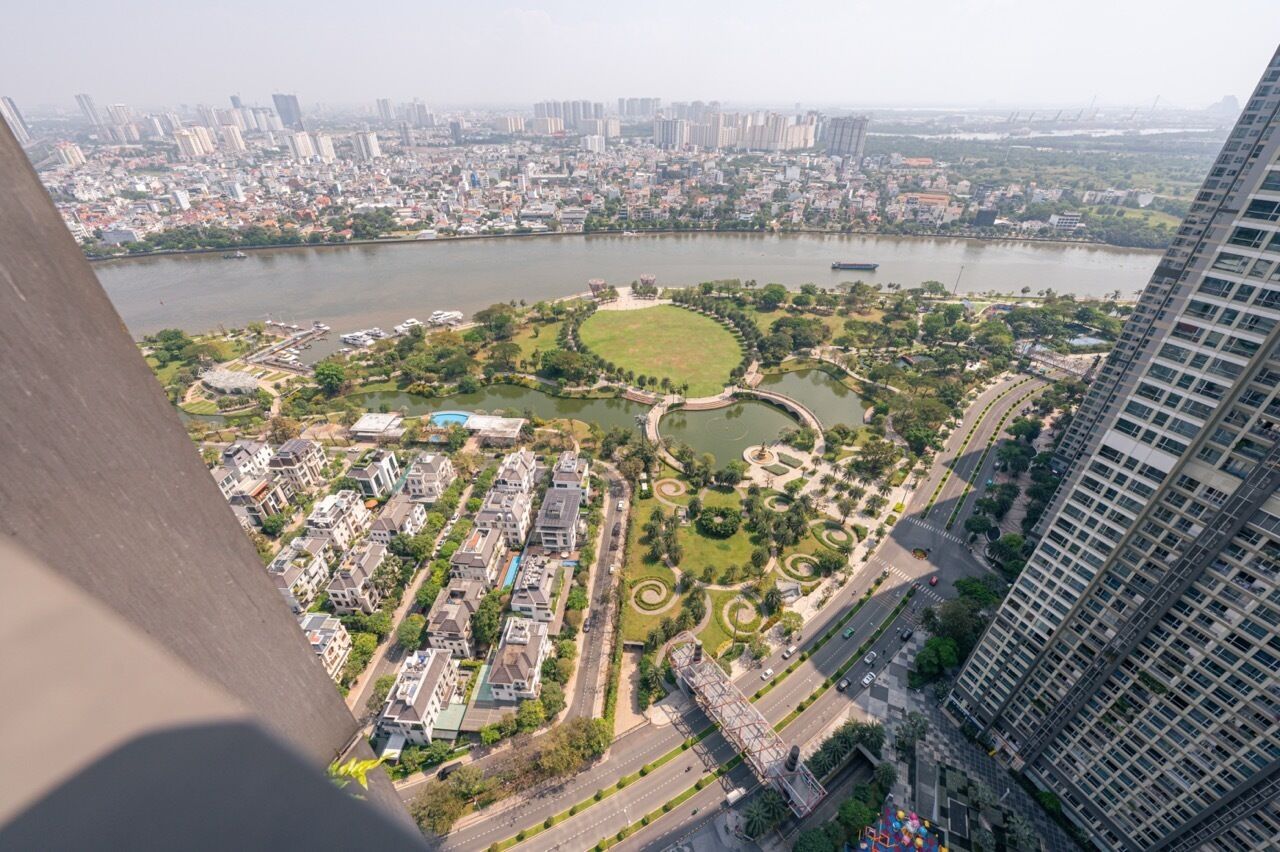 A high-rise building overlooking a park with a river, residential area, and a bridge.