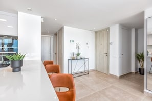 A modern kitchen with a white countertop, a built-in oven, and a dining area with orange chairs.