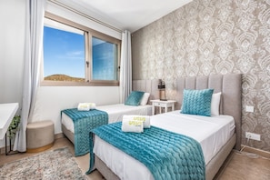 A hotel room with two beds, a window with curtains, a bedside table with a lamp, and a patterned wall.