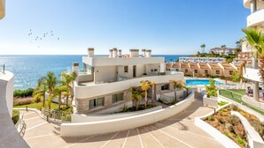A modern resort with a pool, palm trees, and a view of the sea.