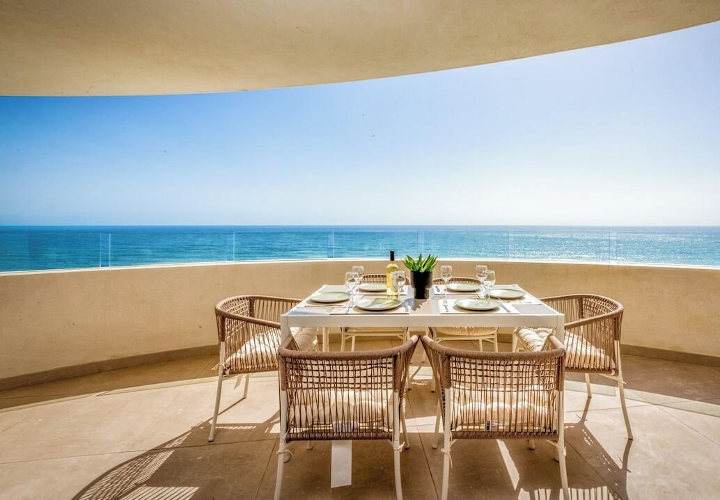 Une table à manger pour quatre personnes, avec des chaises en osier, donnant sur une mer d’un bleu limpide.
