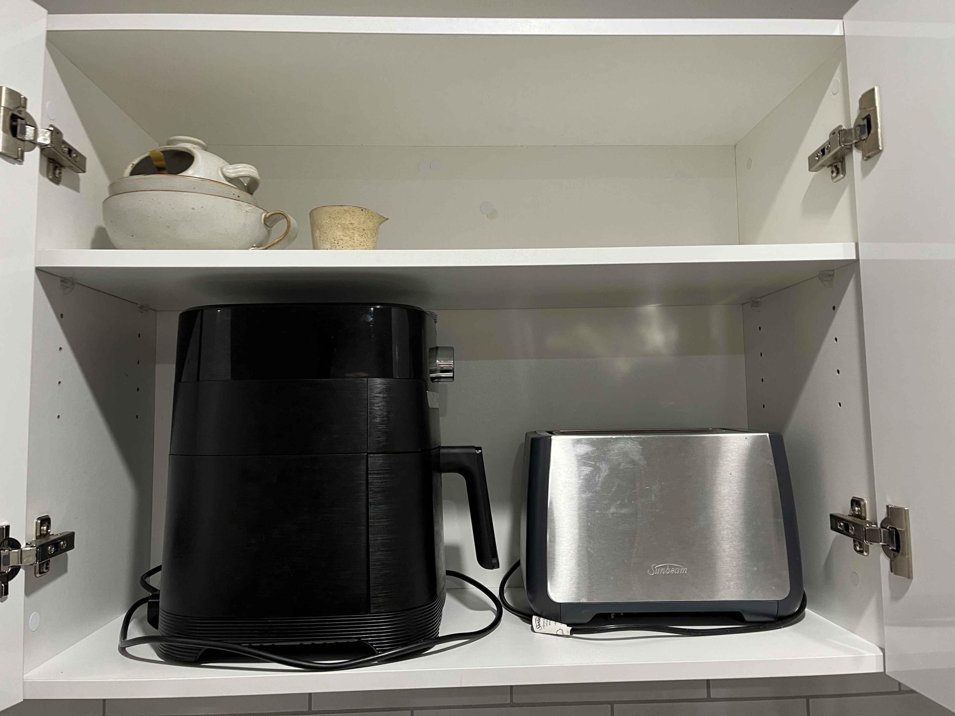 Un armario blanco con una cafetera negra y un tostador plateado en el estante inferior.