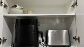 Un armario blanco con una cafetera negra y un tostador plateado en el estante inferior.