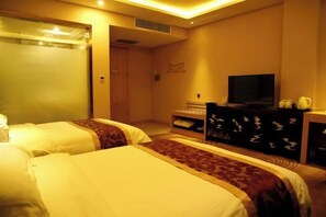 Habitación de hotel con dos camas, televisor, escritorio con computadora y una pequeña zona de estar.