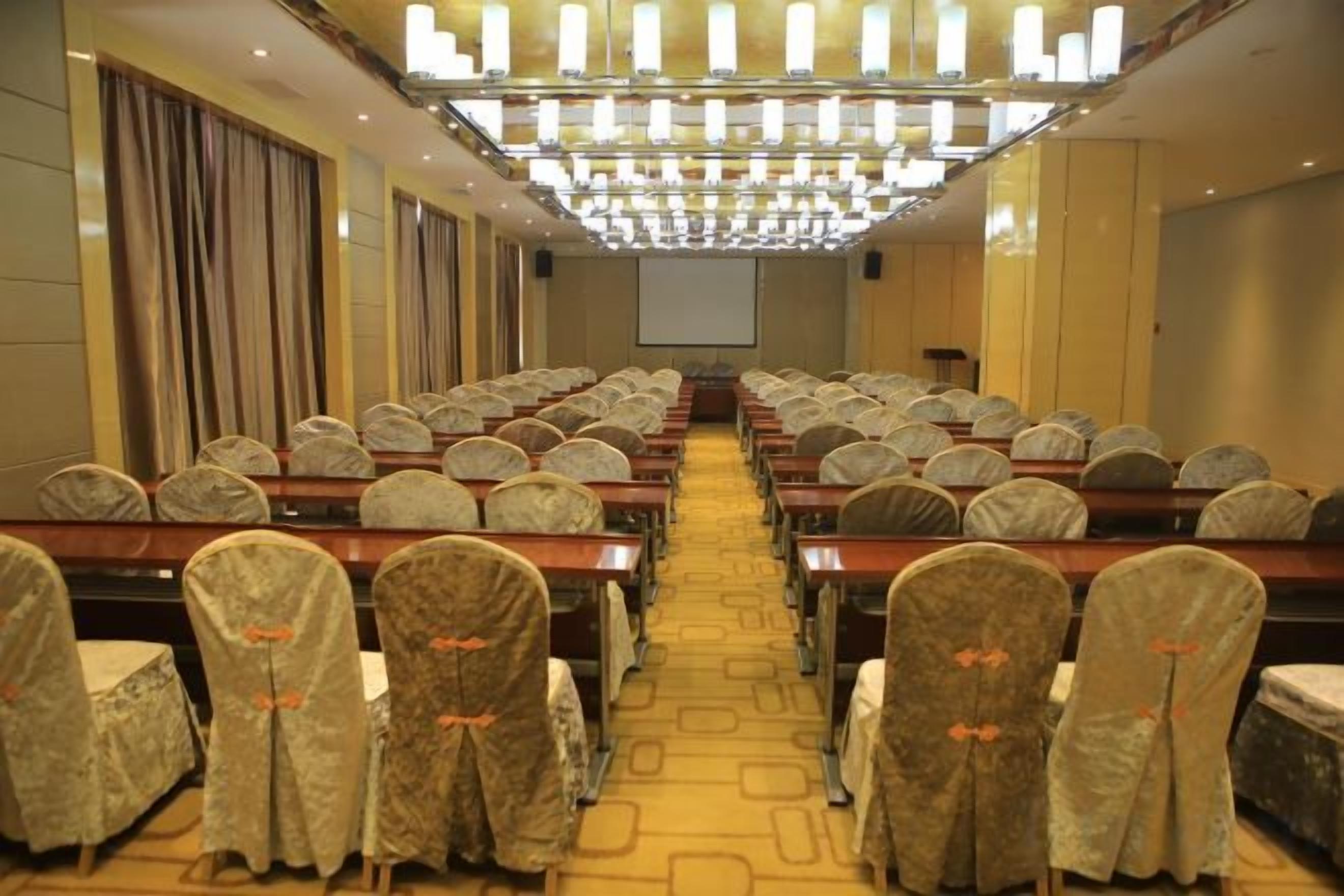 A conference room with rows of tables and chairs, a projector screen at the front, and a chandelier overhead.