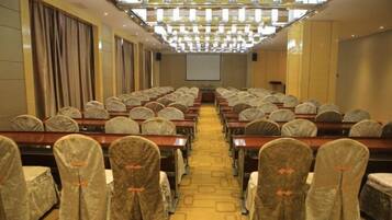 A conference room with rows of tables and chairs, a projector screen at the front, and a chandelier overhead.