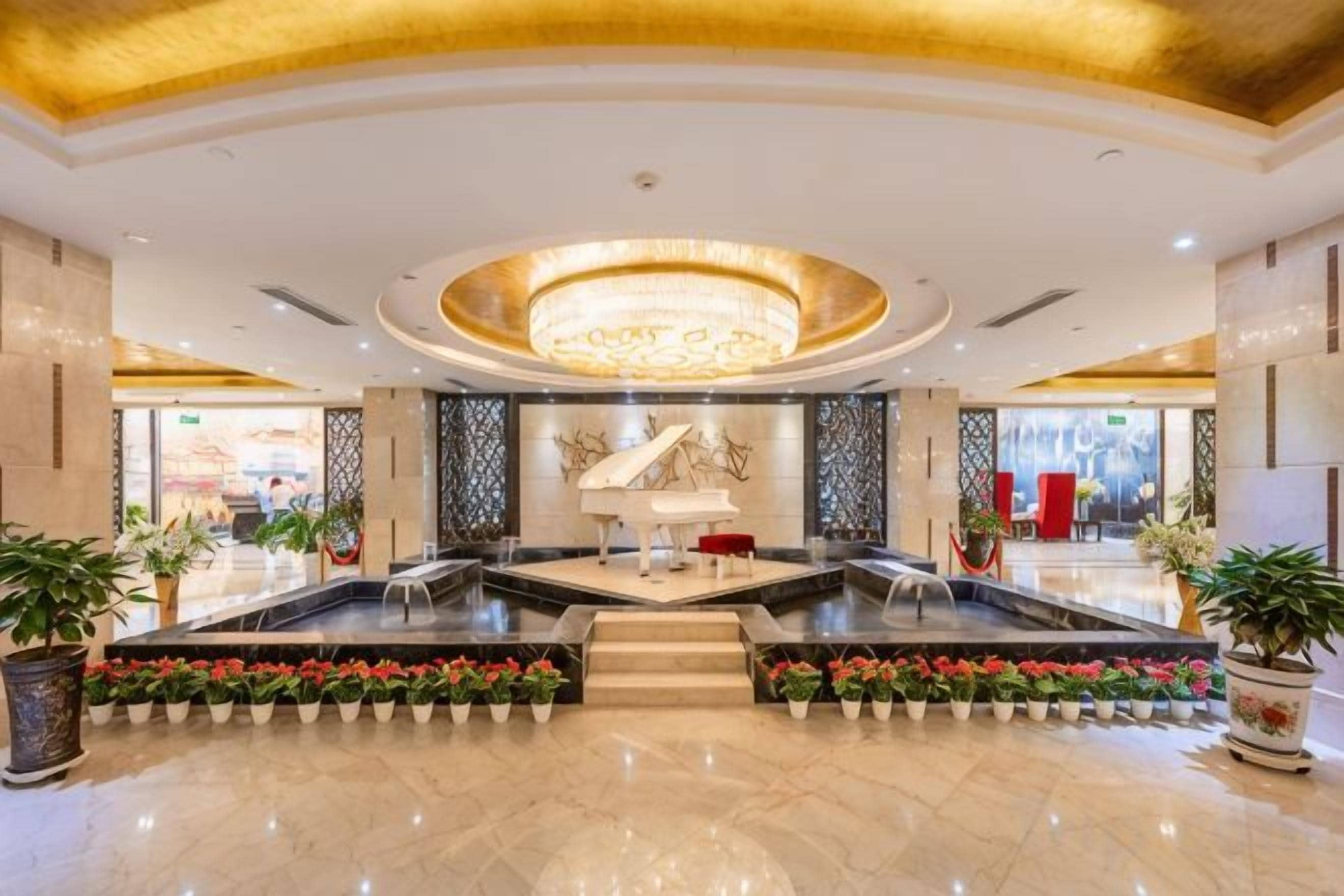 A hotel lobby with a grand piano, a chandelier, and a fountain.