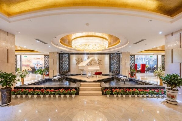 A hotel lobby with a grand piano, a chandelier, and a fountain.
