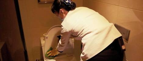 A person cleaning a toilet in a bathroom with a visible trash bin and a framed picture on the wall.