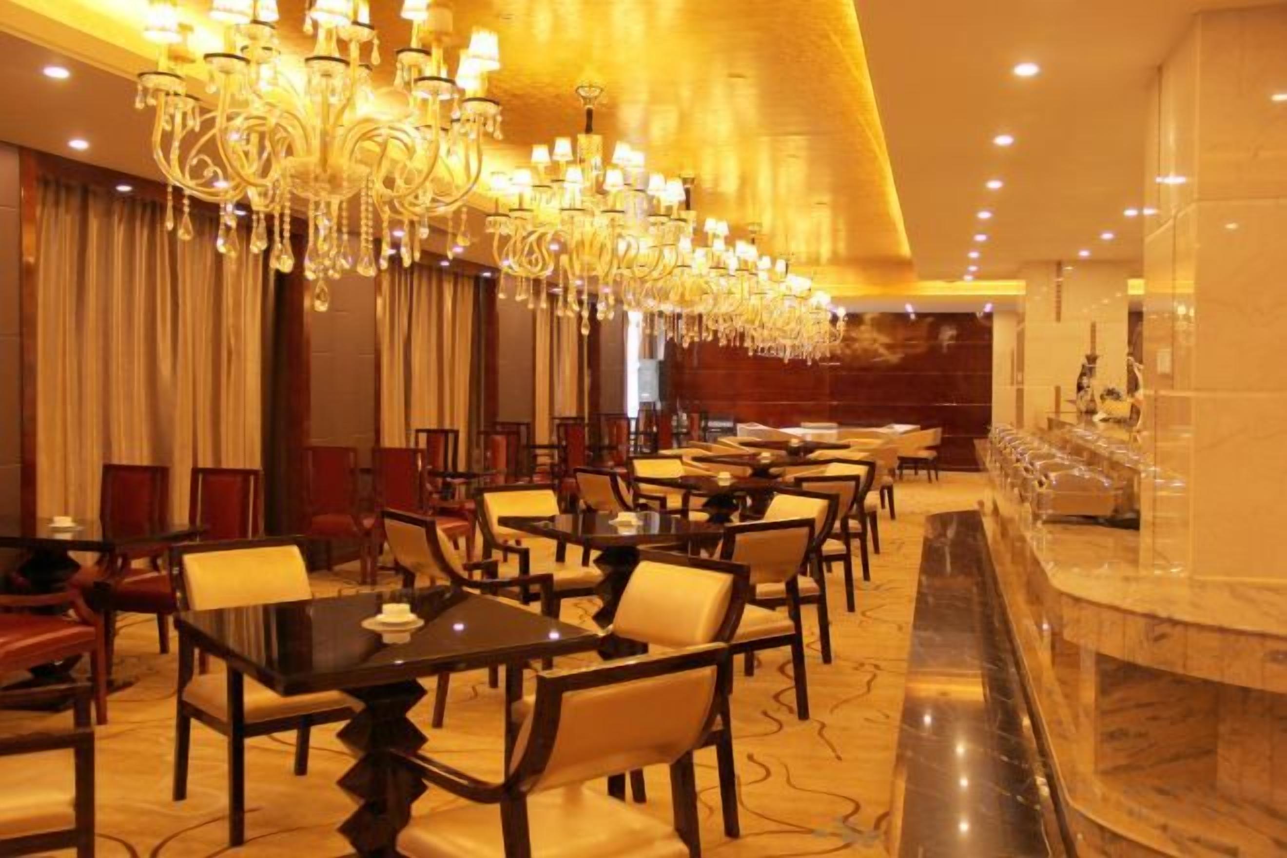 A hotel dining area with multiple tables and chairs, a marble bar, and a large chandelier.