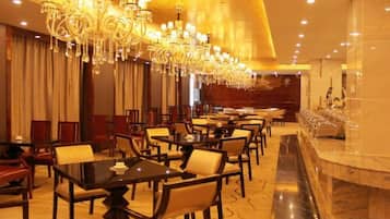 A hotel dining area with multiple tables and chairs, a marble bar, and a large chandelier.