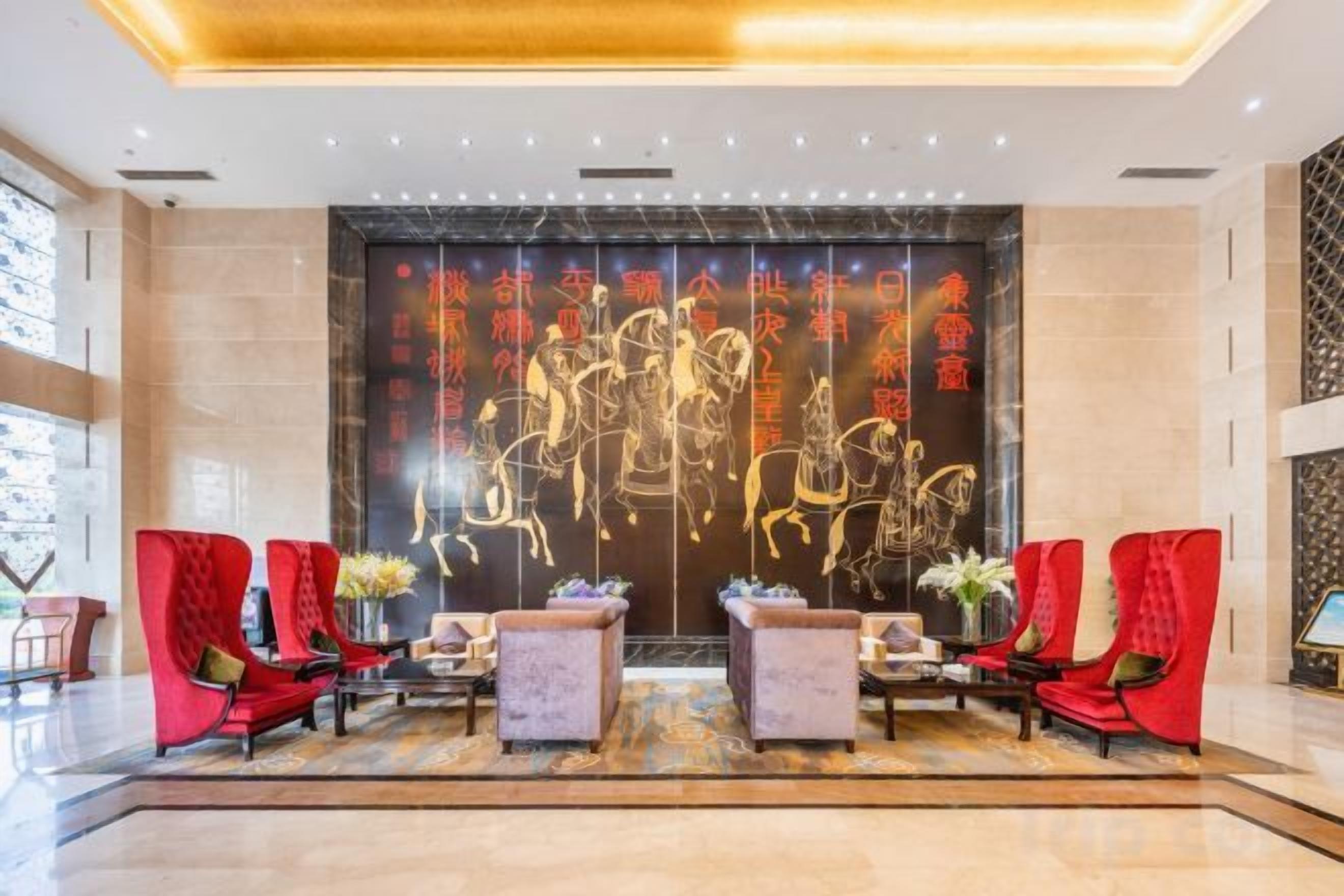 A lobby with a reception desk, red chairs, and a decorative wall with golden script.