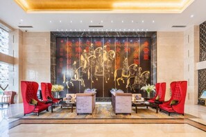 A lobby with a reception desk, red chairs, and a decorative wall with golden script. - Yuyang International Hotel (Gaotai)