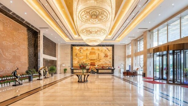 Een ruime lobby met een grote kroonluchter, een receptiebalie en een muurschildering.