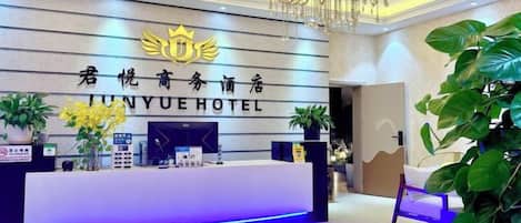A hotel reception desk with a modern design, a chandelier, and potted plants.