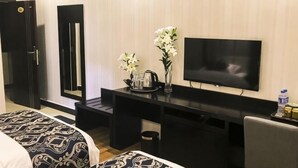 Ein Hotelzimmer mit Bett, Schreibtisch mit Fernseher, Spiegel und Blumen in einer Vase.