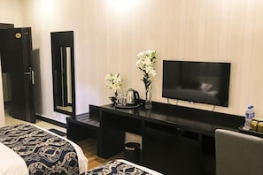 A hotel room with a bed, a desk with a TV, a mirror, and a vase with flowers. - Junyue Hotel (Yuanmou)