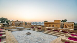 Terraza en la azotea con suelo de piedra y zonas de estar con cojines rojos, rodeada de arquitectura tradicional.