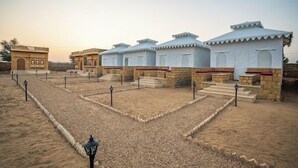 Un resort en el desierto con yurtas y edificios tradicionales, que cuenta con un patio arenoso y senderos de piedra.