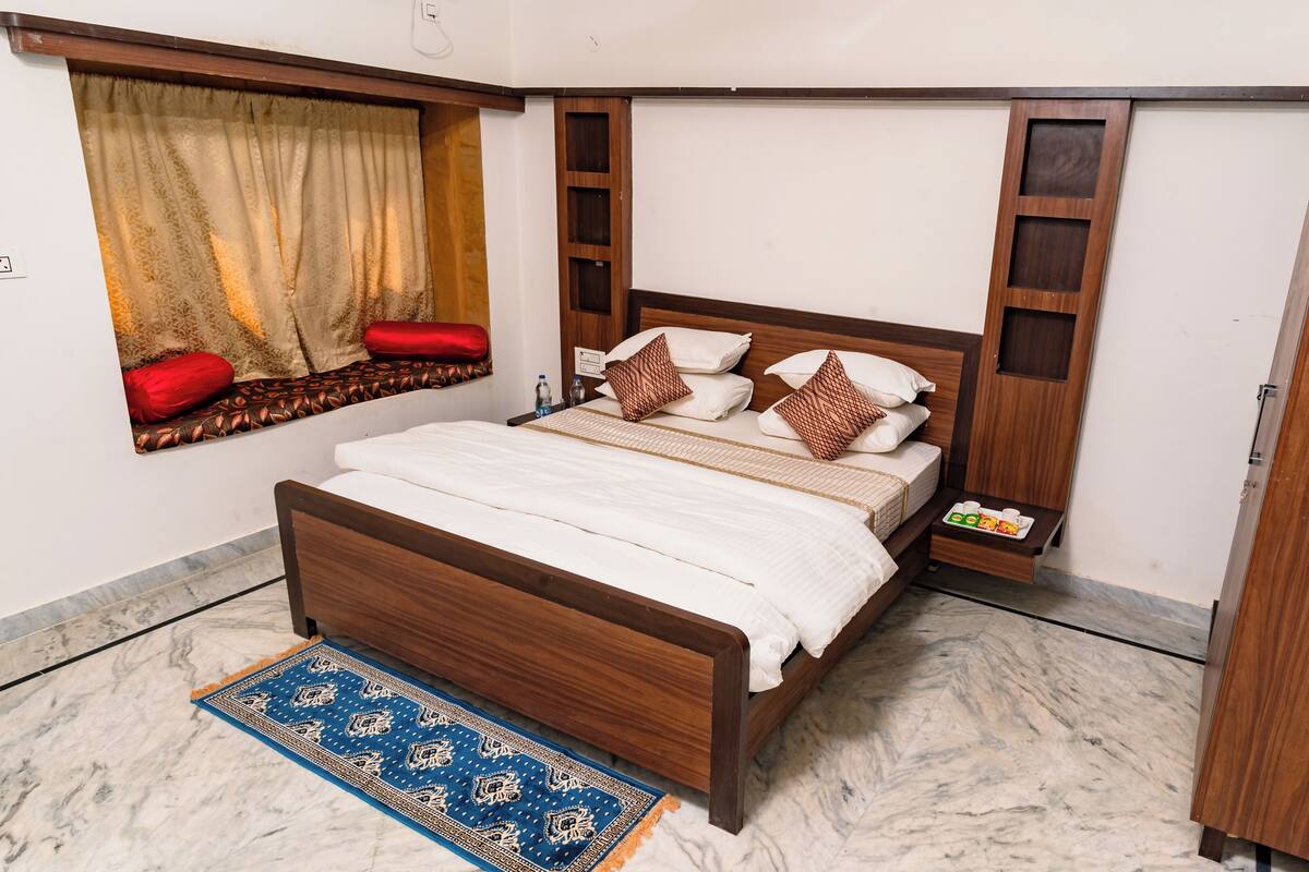 A neatly arranged bedroom with a wooden bed, a window with curtains, a bedside table, and a wardrobe.