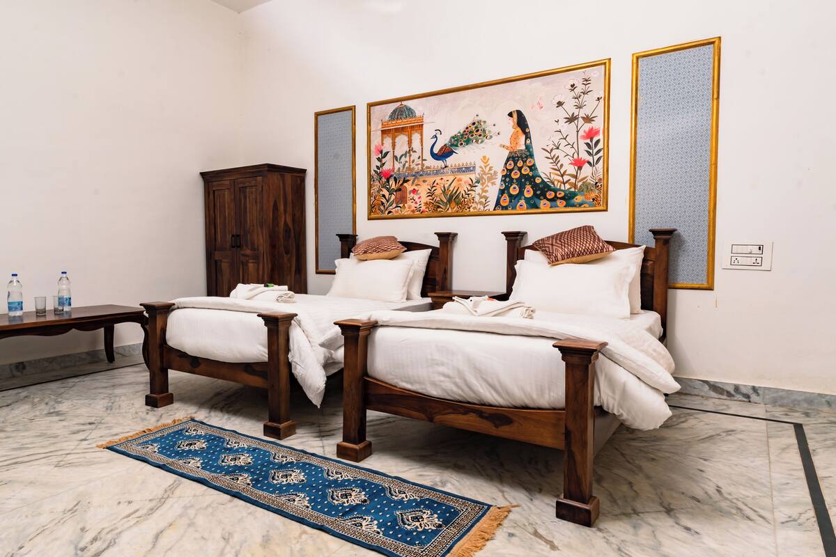 A hotel room with a wooden bed, a marble floor, a blue patterned rug, a wooden cabinet, and a wall with a colorful painting.