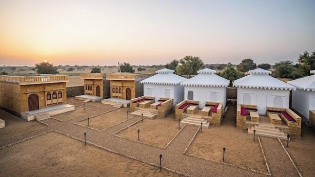 Un resort en el desierto con arquitectura tradicional, que incluye pequeñas tiendas blancas con cojines rojos y un edificio de piedra con ventanas de arco.