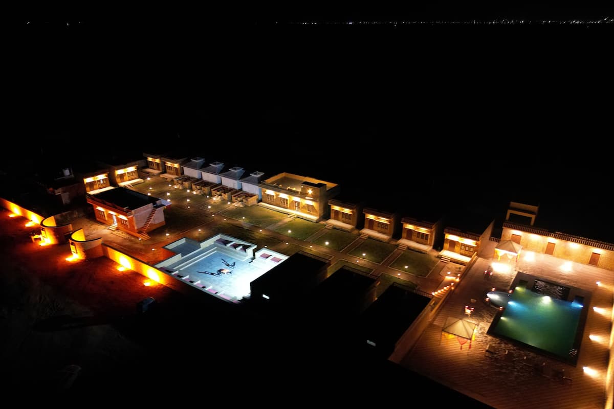 An aerial view of a resort with multiple buildings, a swimming pool, and well-lit areas.