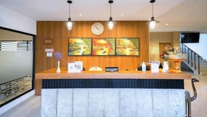 Zona de recepción de hotel con un panel de pared de madera, un reloj y tres cuadros.