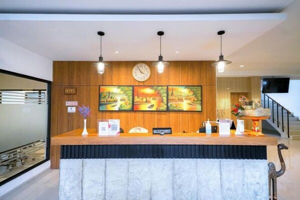 Un mostrador de recepción con un panel de madera de fondo, un reloj y tres obras de arte enmarcadas.