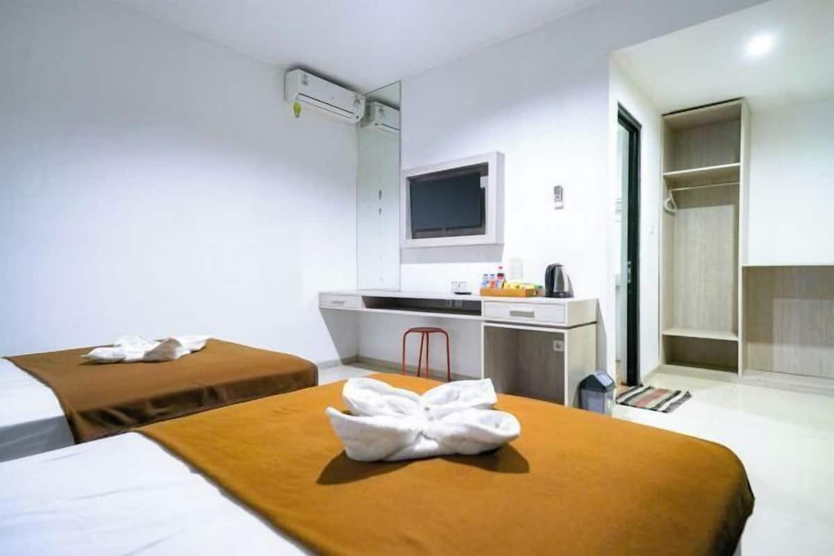 Une chambre d’hôtel avec deux lits, un bureau, un miroir, une télévision et une armoire.