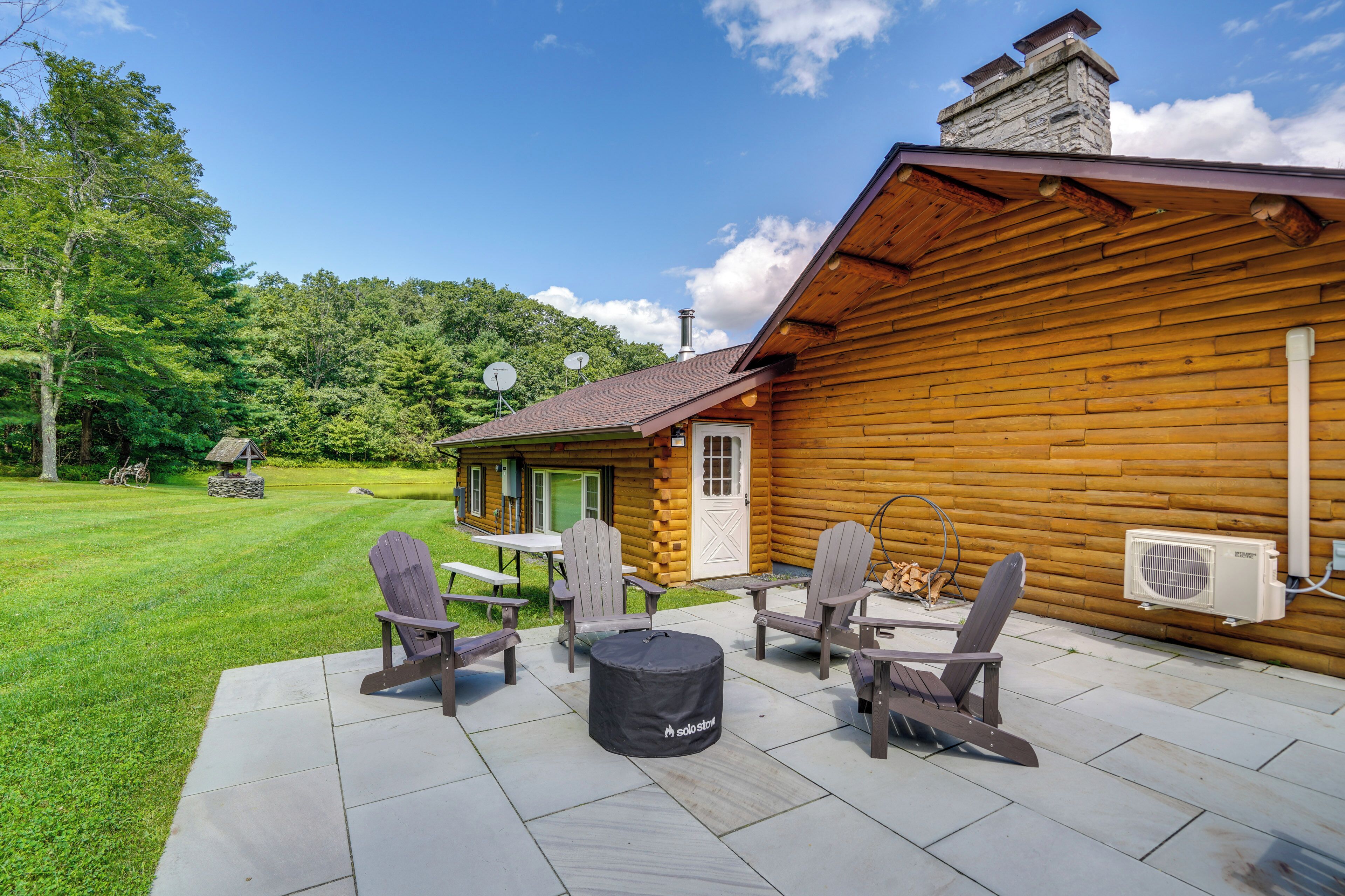 Una cabaña de troncos con un patio que tiene sillas Adirondack y una mesa redonda.